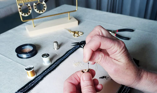 gros plan sur des mains en train de réaliser une boucle d'oreille en perles miyuki