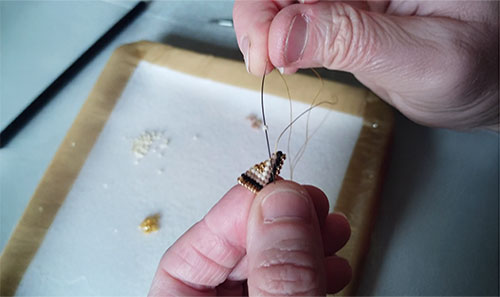 Gros plan sur des mains tissant une boucle d'oreille avec un fil, des aiguilles et des perles miyuki
